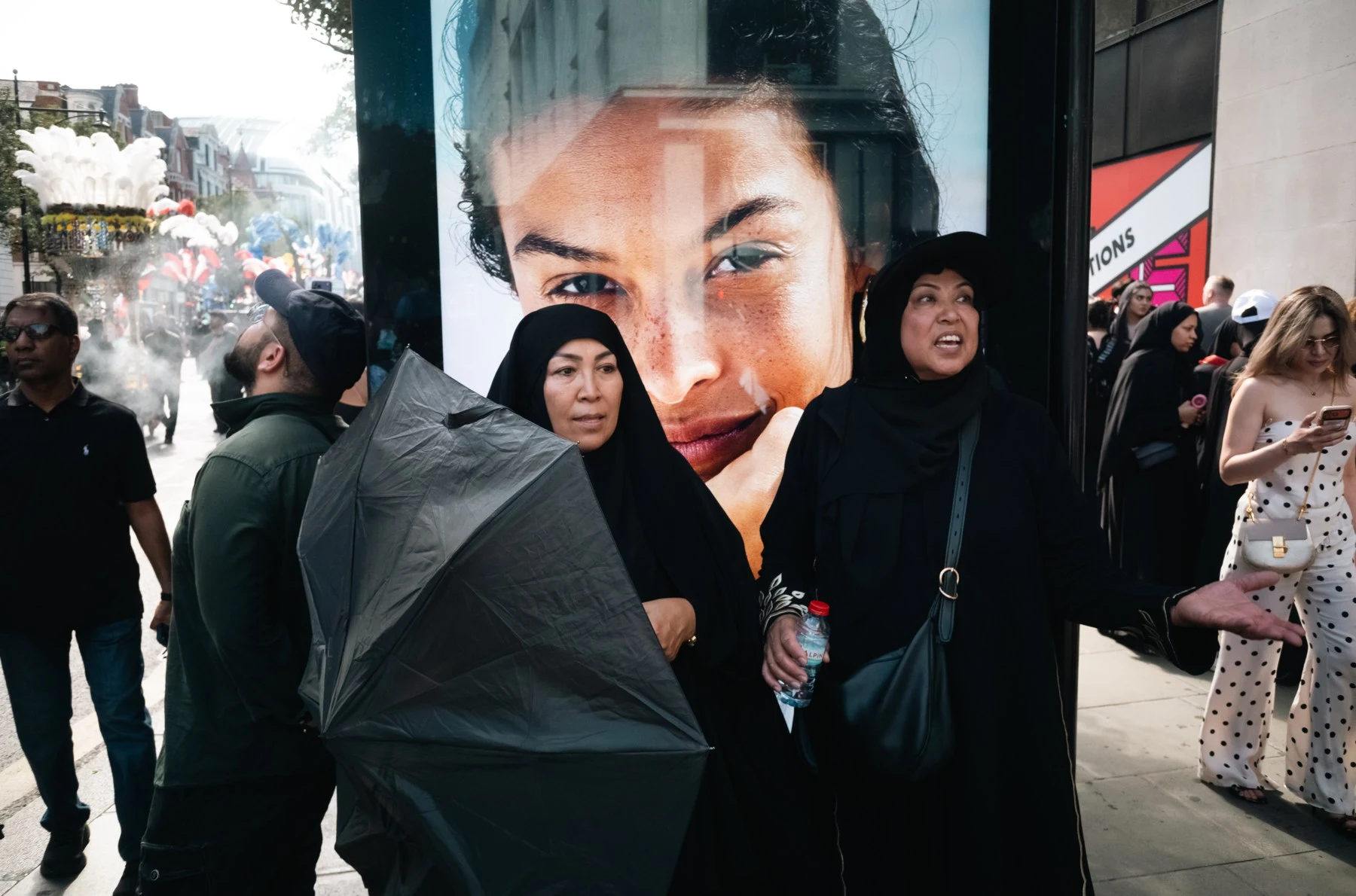 Pedestrians pass an advertising portrait with an oversized face.