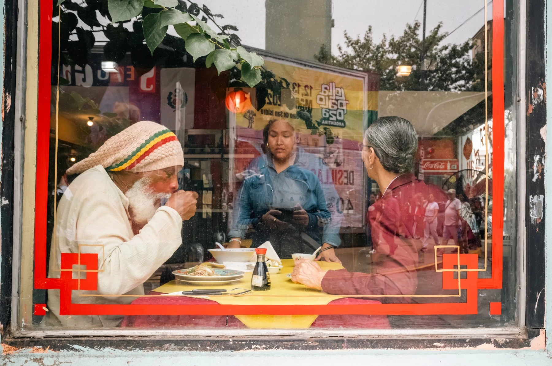 People eating behind a red-framed restaurant window.